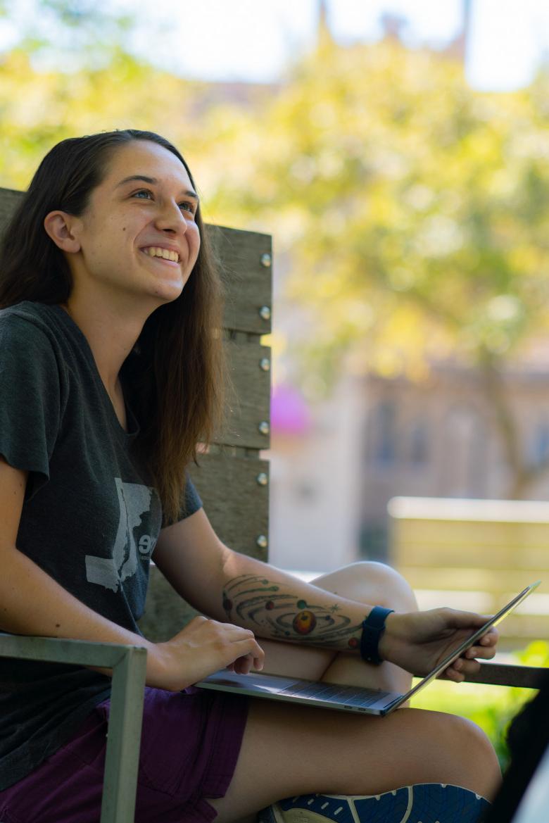 student sits on a bench in the poetry garden with a laptop 和 green foliage around